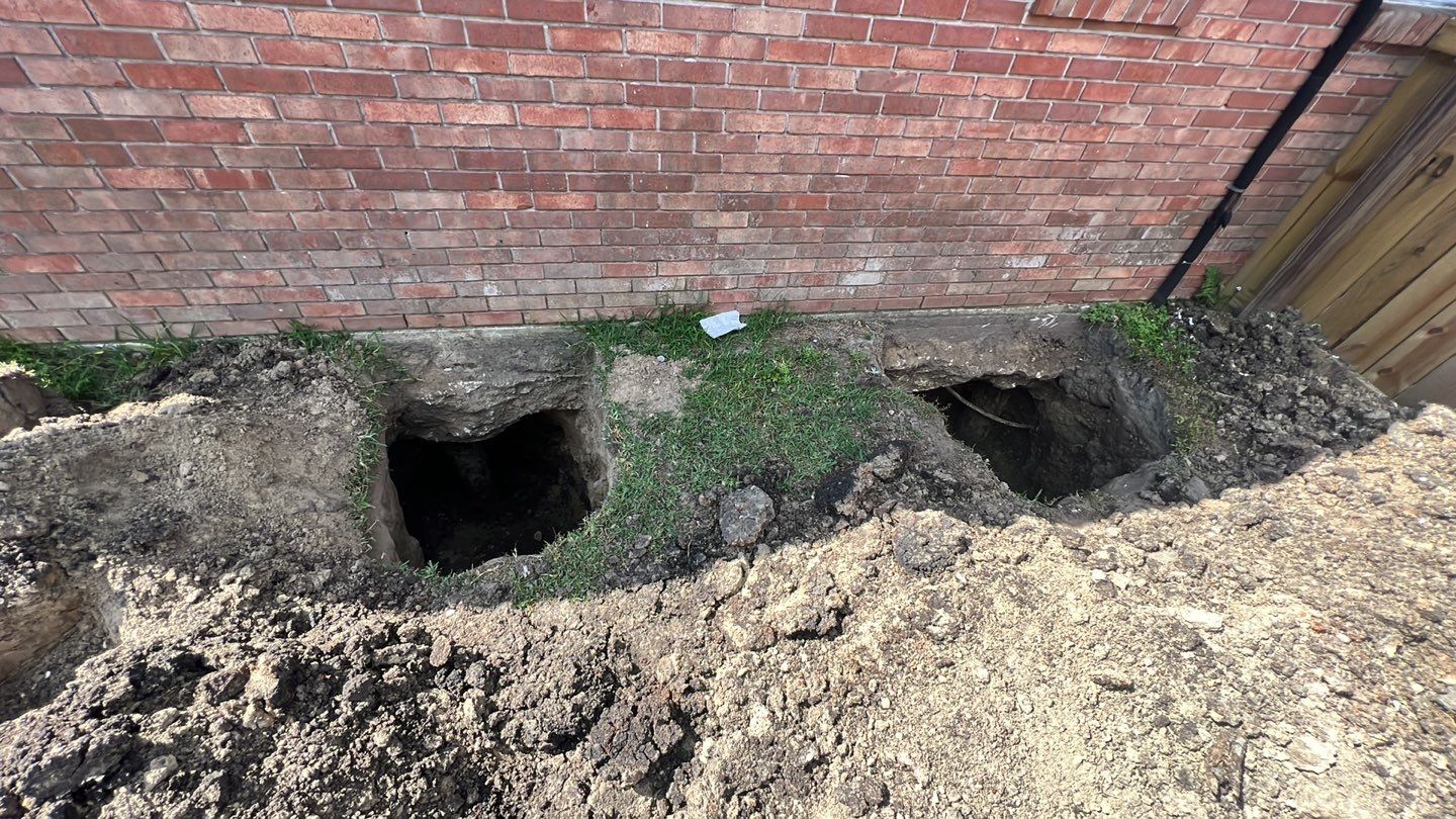A foundation repair hole next to a brick house.