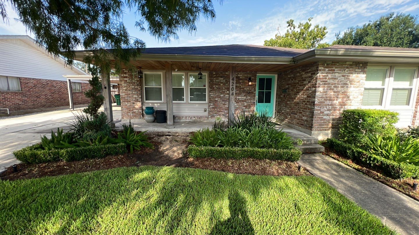 A small house with a green lawn and bushes needing foundation repair.