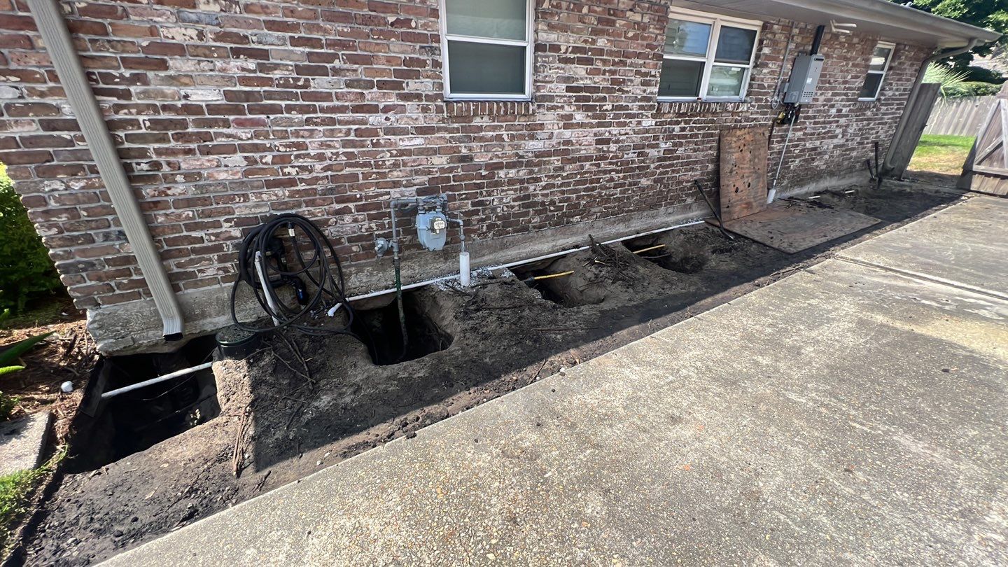 A house undergoing foundation repair with a hose and pipe in front of it.