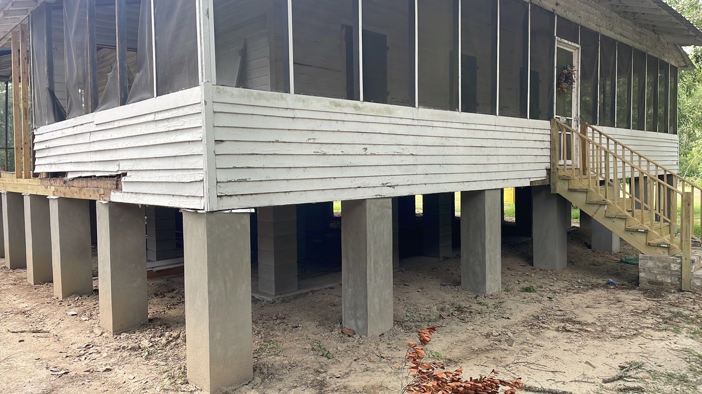 A house with a porch and steps in the middle of the yard undergoes foundation repair.