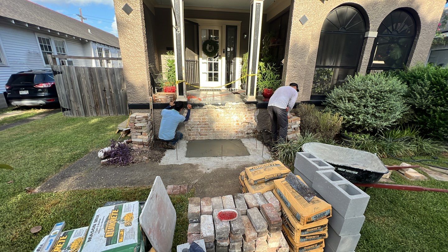 A man is laying bricks on the front steps of a house undergoing foundation repair.