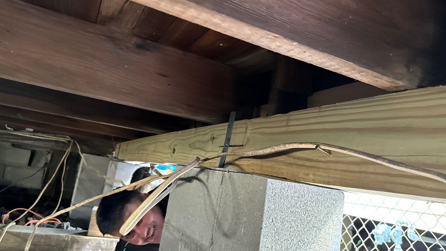 A man is working on a wooden beam under a house.