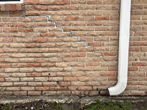 A damaged brick wall adjacent to a white pipe, indicating potential need for foundation repair.